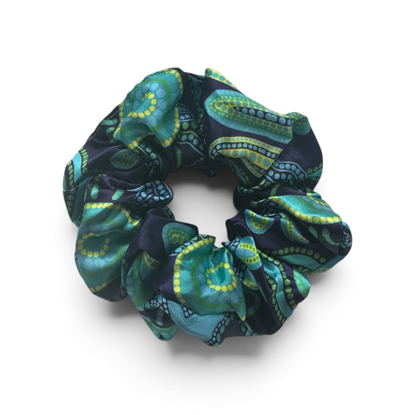 A fabric hair scrunchie featuring a detailed paisley pattern in teal, green, and yellow on a dark navy background, shown on a clean white studio background.