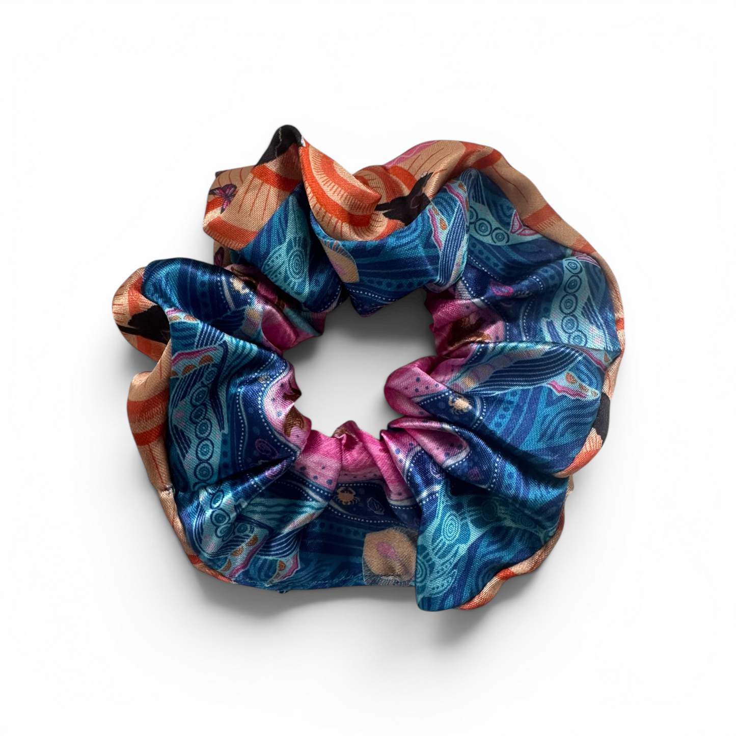 A silk scrunchie with an intricate, multicolored bohemian-style pattern featuring blue, pink, orange, and gold, displayed on a clean white background.