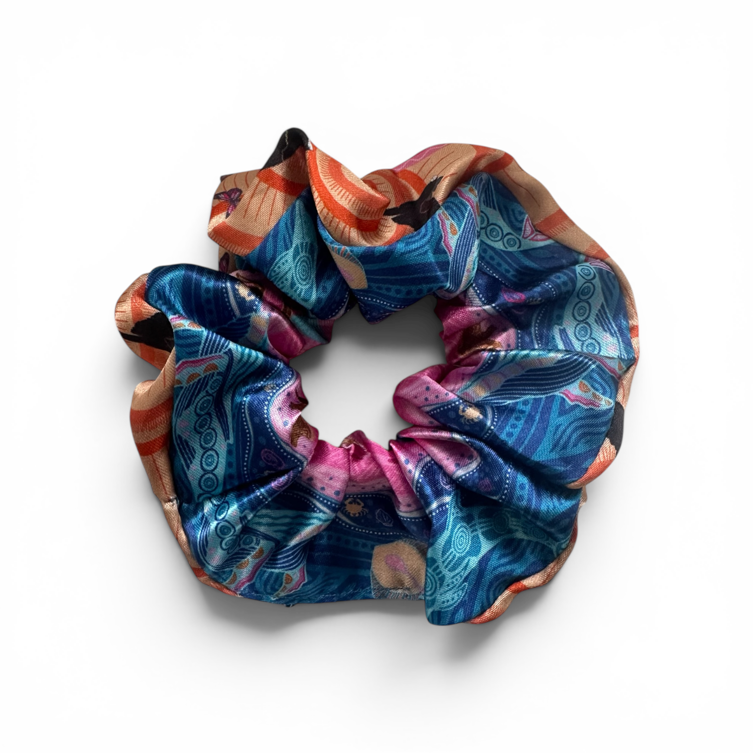 A silk scrunchie with an intricate, multicolored bohemian-style pattern featuring blue, pink, orange, and gold, displayed on a clean white background.