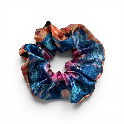 A silk scrunchie with an intricate, multicolored bohemian-style pattern featuring blue, pink, orange, and gold, displayed on a clean white background.