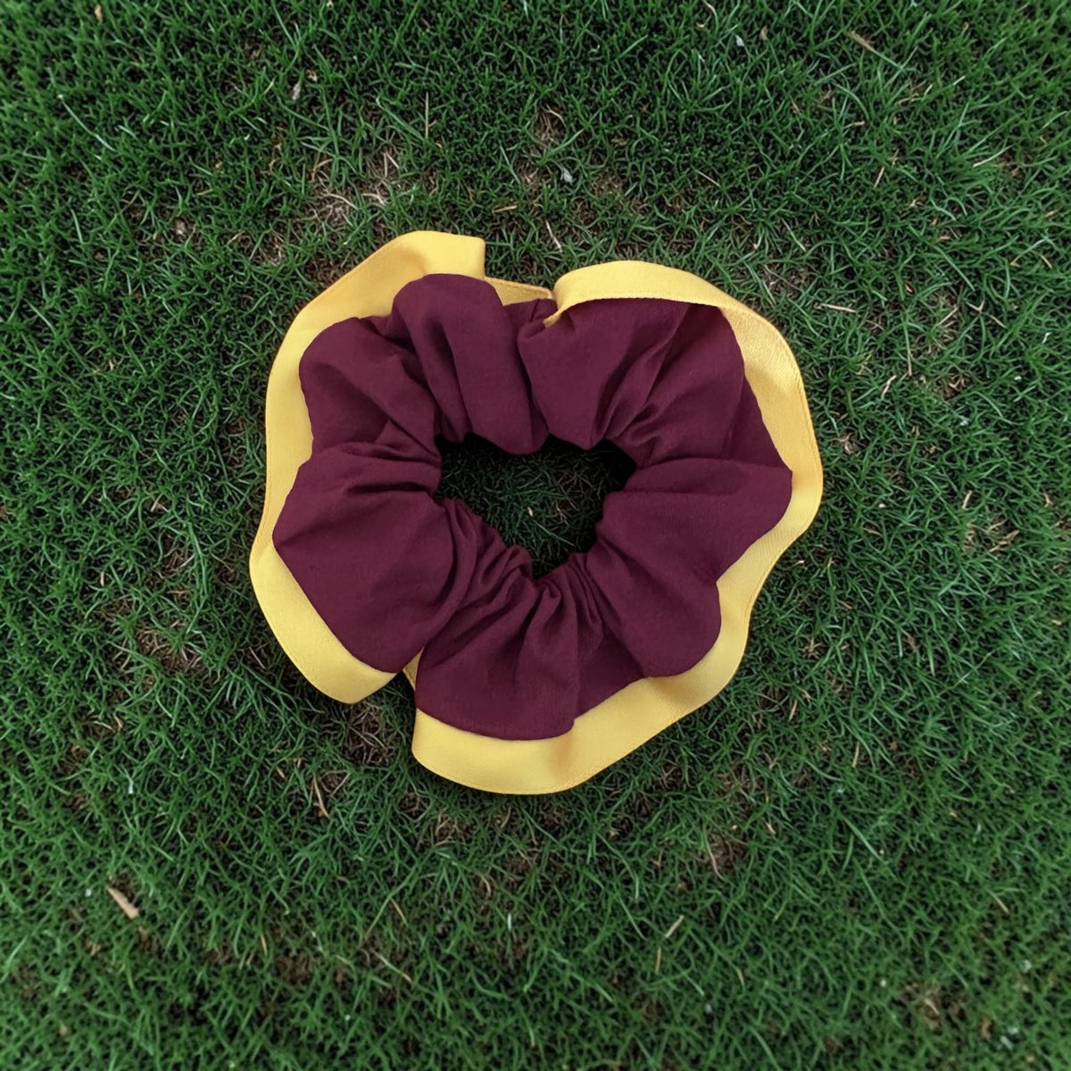 A fabric scrunchie with a maroon center and yellow outer flange, placed on green grass.