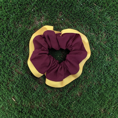 A fabric scrunchie with a maroon center and yellow outer flange, placed on green grass.