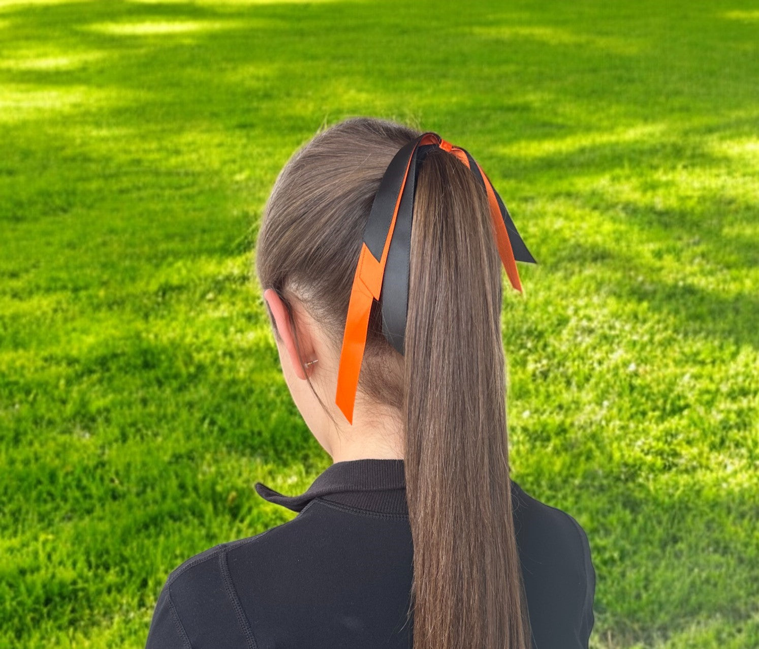 Person with a ponytail wearing black and orange ribbons against a grassy background