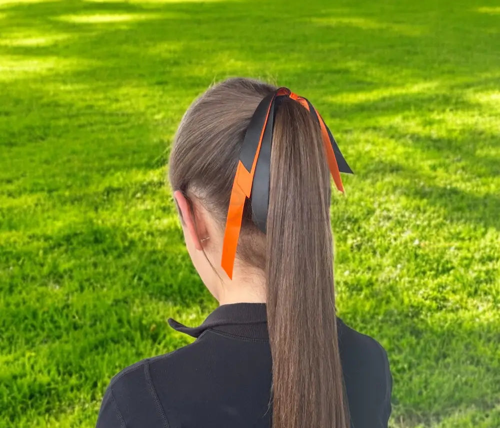 Person with a ponytail wearing black and orange ribbons against a grassy background